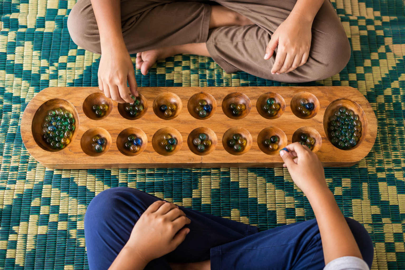 Two people playing Congklak on a wooden board